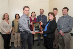 The outgoing OMV-SfN president, James Olson passes the 2014 SfN Chapter-of-the-Year Award plaque to the incoming president for 2015-2016, Kathleen Killian at the 2015 OMV-SfN winter meeting. Past presidents of OMV-SfN in the back row are (left to right) Lori Isaacson, Joyce Fernandez, Phyllis Callahan, Kim Seroogy, Michael Hennessey, andMark Baccei.